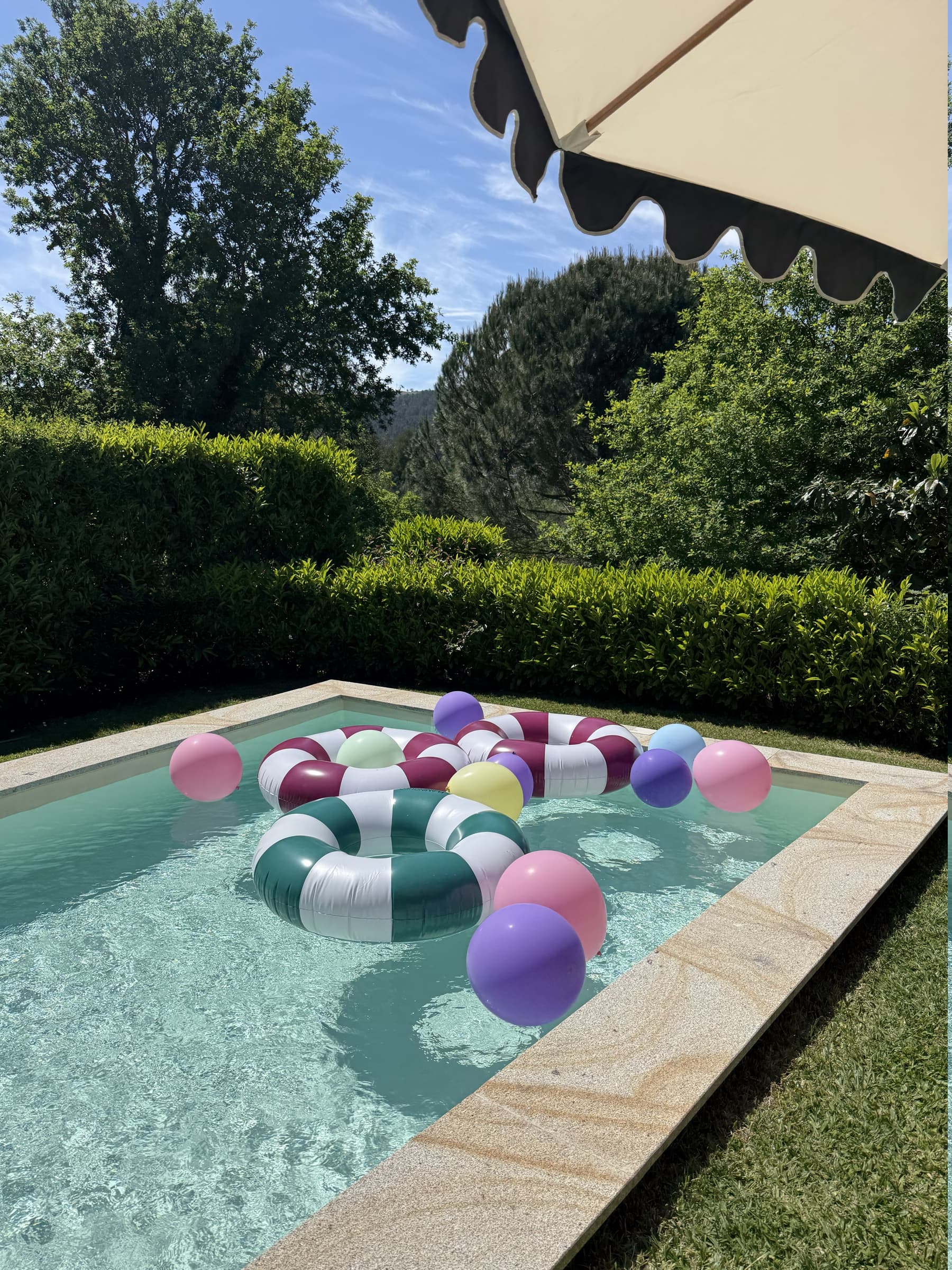 Boias coloridas na piscina, com a sebe alta e os montes do Minho ao fundo.